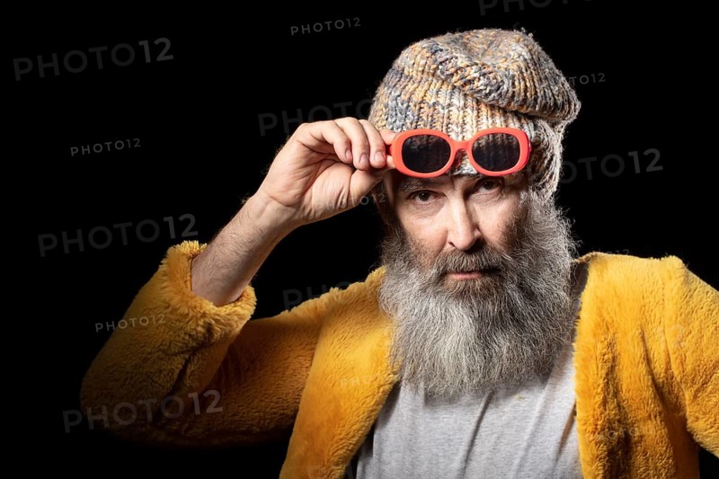 An elderly man with a grey beard wearing a knitted hat and a bright yellow fur coat. Fashionable man on a black background