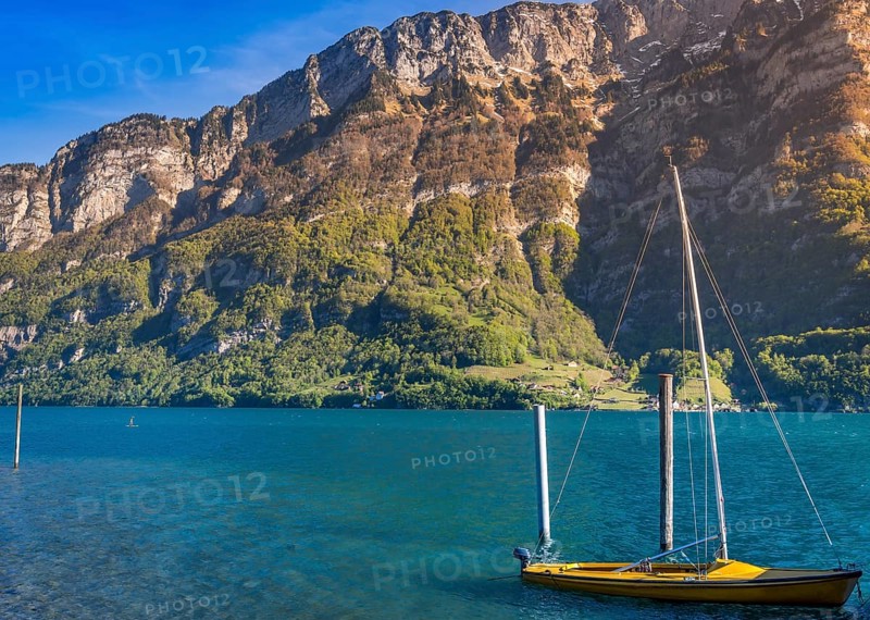 Image taken in the Murg Ost village, Switzerland, presenting a small boat on the Walensee lake in the morning sunlight, surrounded by the Swiss Alps mountains