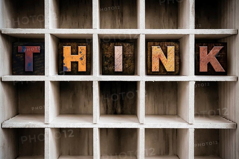 The word THINK written in vintage ink stained wooden letterpress type in a partitioned printer's drawer