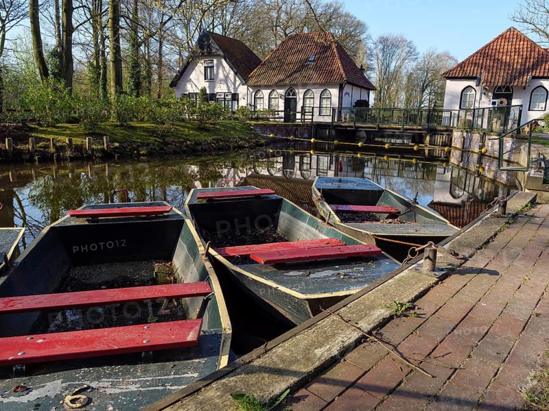 Boats in a pond in front of reflective houses with red roofs and white walls, surrounded by trees, winterwswijk, gelderland, Netherlands