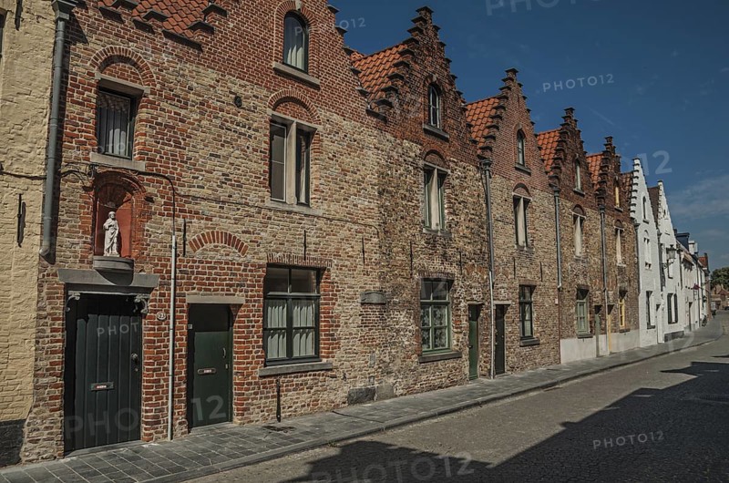 Brick facade of old houses with a blue sunny sky in an empty street of Bruges. With many canals and old buildings, this graceful town is a World Heritage Site of Unesco. Northwestern Belgium