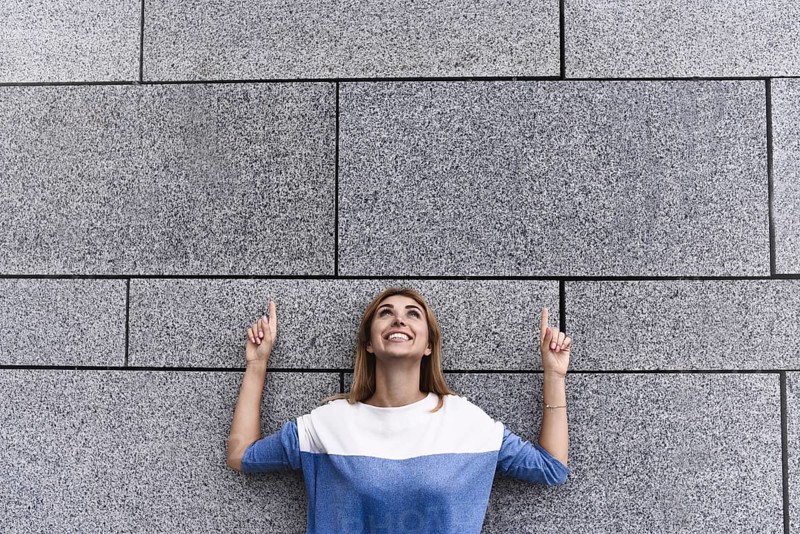 Cheerful girl at the street, show a big sale, or nice offer. Advertise concept. People, travel and tourism, woman on city street and girl show with her fingers something over gray wall background