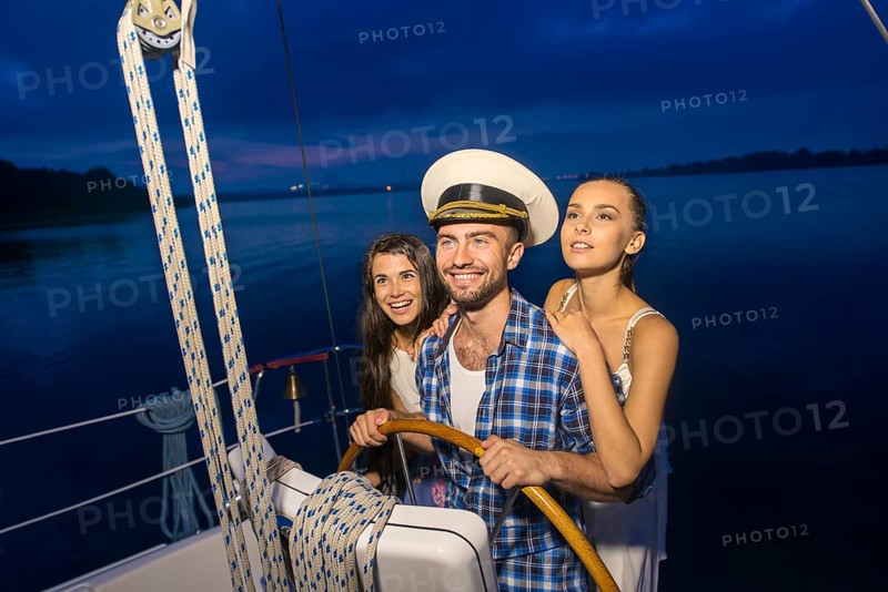 Captain with girls on the yacht. Night cruise on the yacht. Friends traveling by yacht on the river. Holiday on a yacht