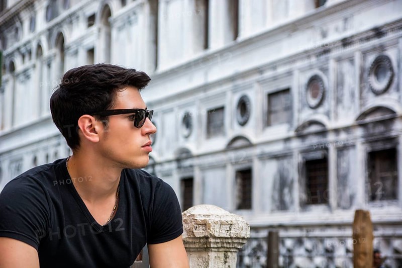 Portrait of Attractive Dark Haired Young Man Leaning Against Railing on Foot Bridge Over Narrow Canal in Venice, Italy