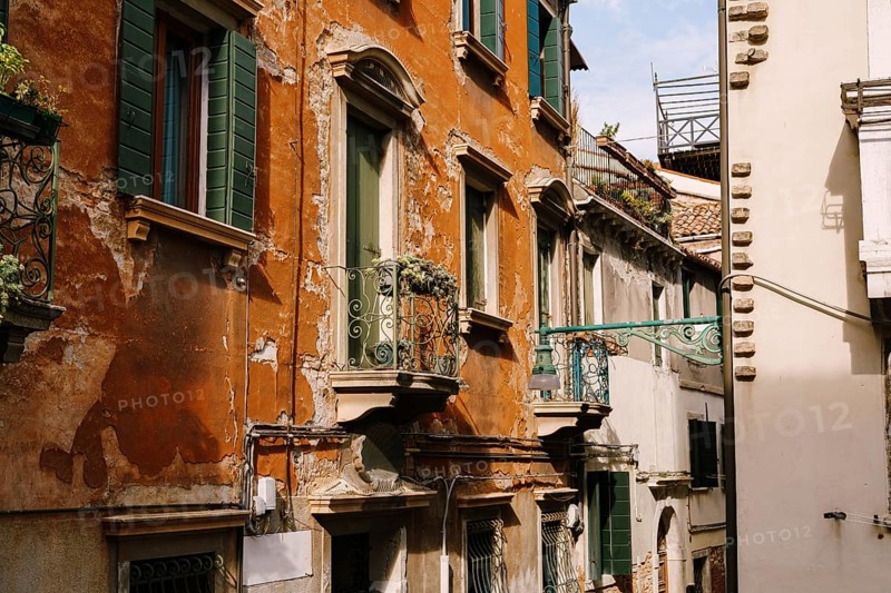 Close-ups of building facades in Venice, Italy. Green wooden door at bottom of brick house. Balcony with a forged fence. An old street lamp on the wall of an apartment building
