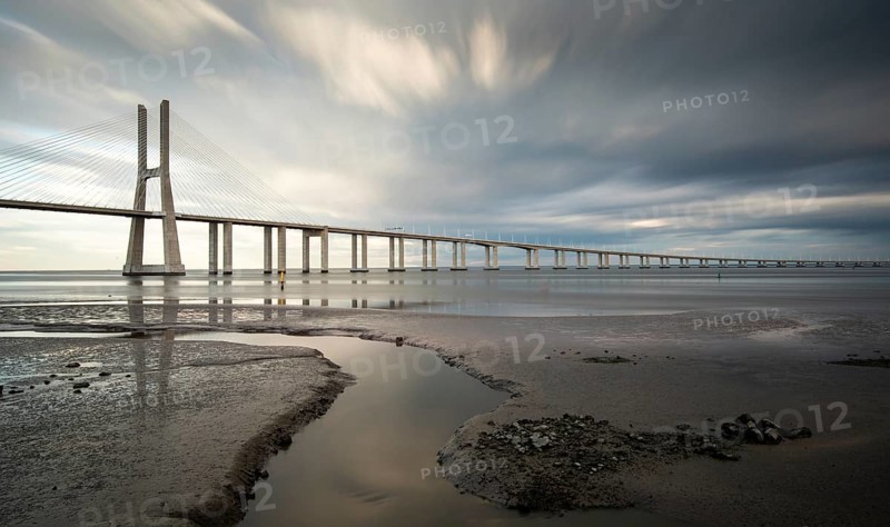 Vasco da Gama Bridge at sunset with dramatic cloudy sky in Lisbon Portugal. Long exposure photograph