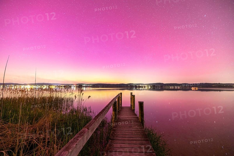 A wooden footbridge leads over a calm lake under a sky with aurora borealis, Reichenau, Lake Constance, Baden-Württemberg, Germany