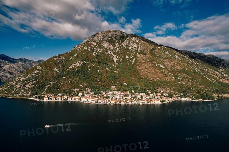 Boat sails along the Bay of Kotor against the backdrop of the coast of Perast at the foot of the mountains. Montenegro. Aerial view.