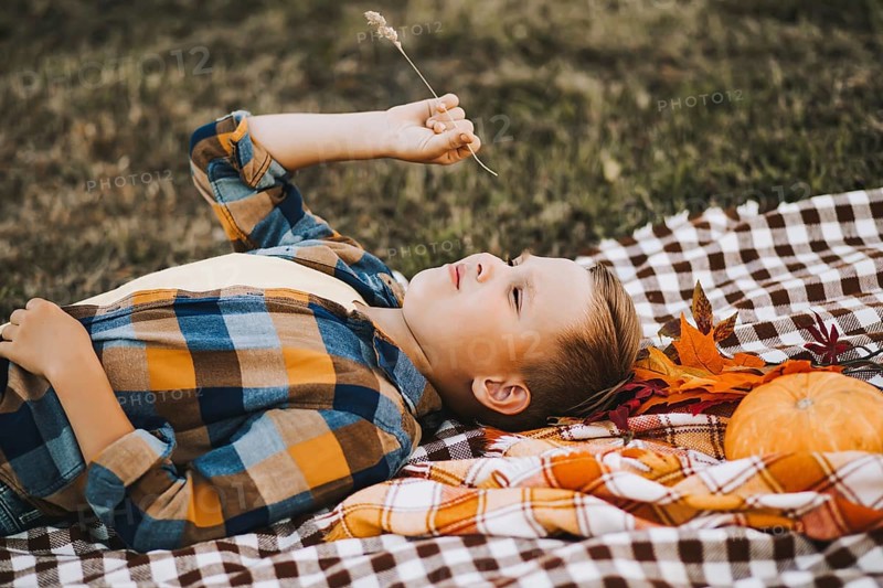 Kid boy lies near a river, pond or lake and smiling. Autumn season. Happy childhood