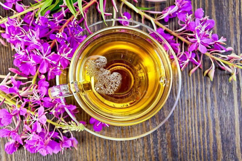 Herbal tea in a glass cup, fresh flowers fireweed against the backdrop of wooden planks on top
