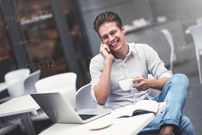 Handsome caucasian young man with phone working on laptop and smiling while enjoying coffee in cafe