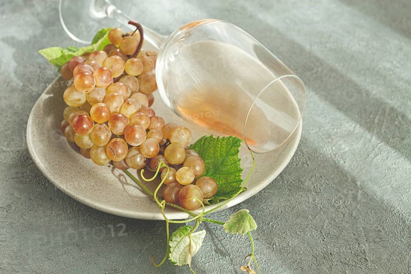 A branch of white grapes, on a gray plate, with a glass of white wine, top view, natural light, food concept, no people