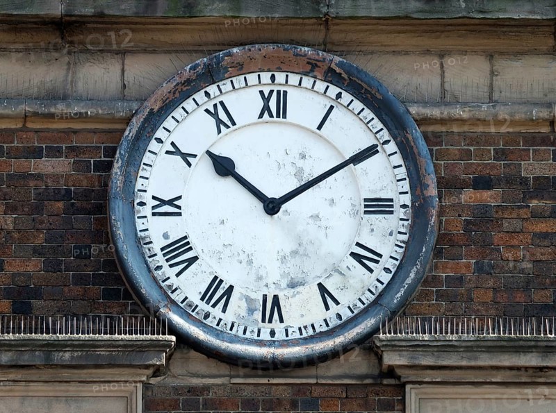 Old round clock on the brick wall of a building with roman numerals with hands at ten past ten