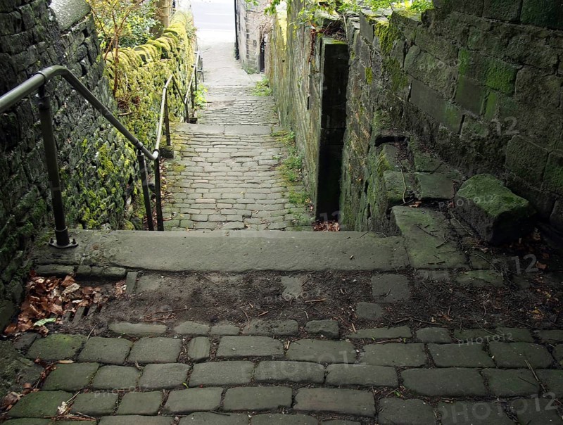 Old outdoor stone steps in dark alley with cobblestones and moss growing on the walls