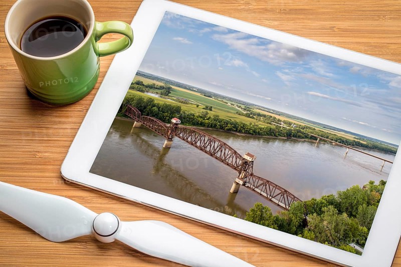Historic railroad Katy Bridge over Missouri River at Boonville - reviewing aerial image on a digital tablet with a cup of coffee