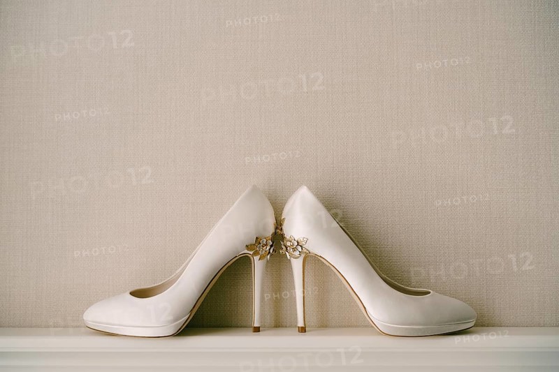 White women's shoes with high pointed heels, with a pattern of flowers, on a gray background.