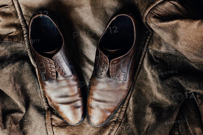 Brown leather shoes placed on a rustic jacket, exuding a vintage and worn aesthetic