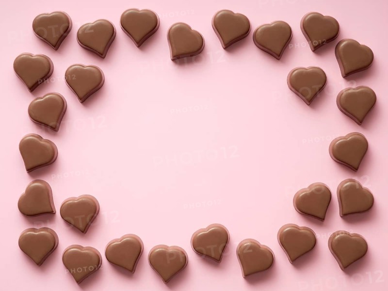 Frame of romantic chocolate confections in heart shapes on pastel pink background. Canvas with heart chocolate sweets with copy space. Valentines day background