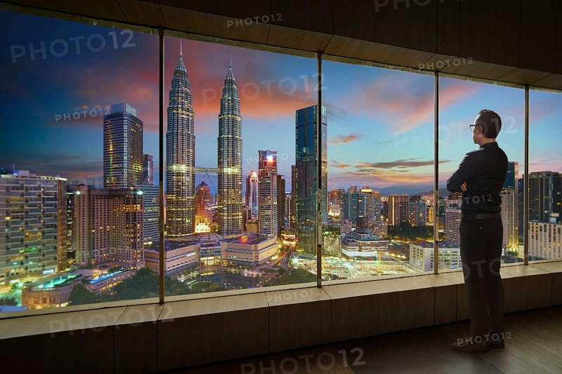 Businessman looking and thinking front of a window office with modern city skyline . Evening scene