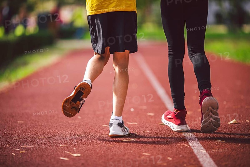 Close-up of the legs in trainers of two children on the running track in the stadium, back view. Boy and girl running on red jogging track in park. Schoolchildren in physical education running around the stadium