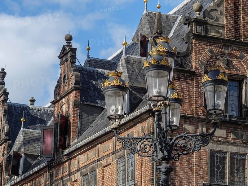 Historic building with ornate roof edges, in the foreground a decorative lantern under a slightly cloudy sky, nijmegen, netherlands