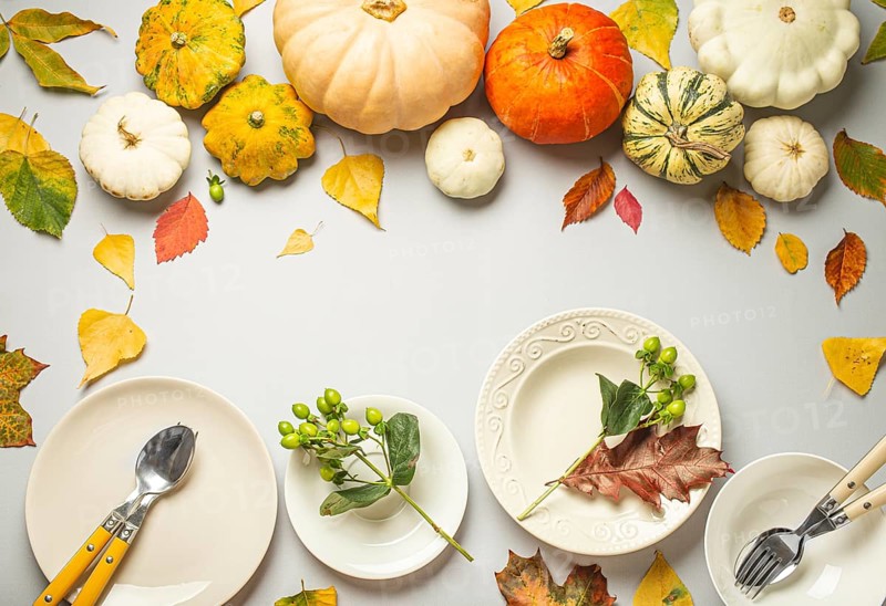 Thanksgiving festive table composition with different colourful pumpkins, autumn leaves, empty plates with cutlery on light grey background table ready for party and celebration. Space for text, food photography, food photography