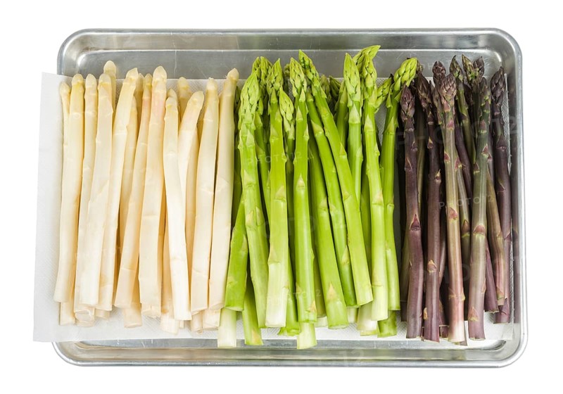 White, green and purple asparagus on a baking tray on a white background