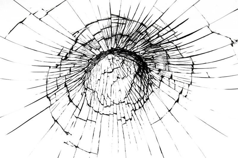 A crack on a broken glass mirror on a black background lines fragments bullet hole
