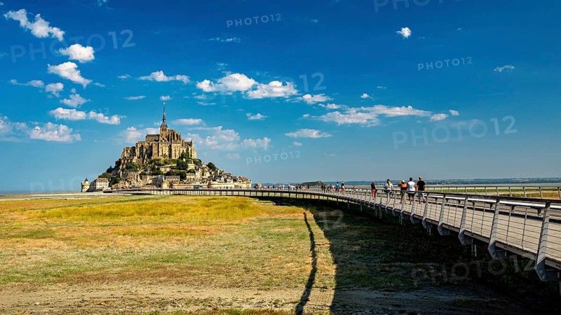 Mont Saint-Michel in summer with a pedestrian bridge in the foreground and blue sky, Mont Saint Michel in Normandy, France