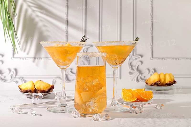Summer party concept. Lemonade royal cocktail, martini or punch made of tequila, rum and vodka with pineapple slices, orange, ice and rosemary. Diet drink for bar or cafe advertising, restaurant menu