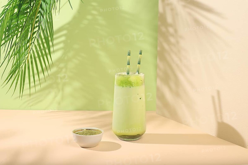 Green tea matcha latte in a glass with bamboo tubes on a modern light background with palm leaves.Traditional Indian drink rich in antioxidants, used for weight loss and treatment, selective focus