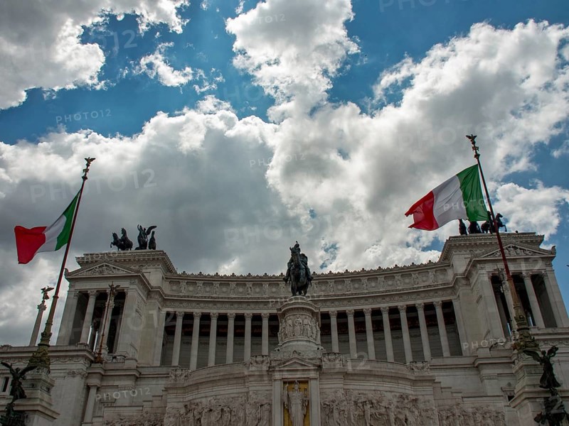 Monumental building with two Italian flags and equestrian statue under a cloudy sky, Rome, Italy