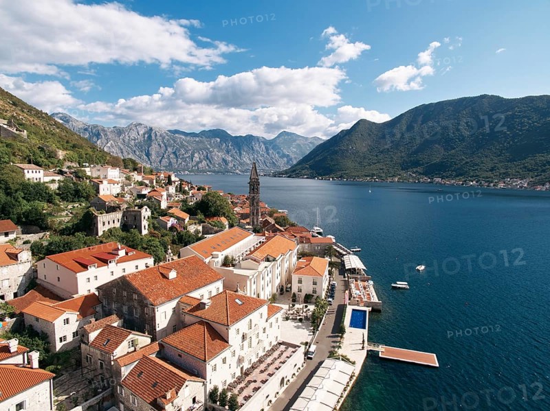 Old houses with red roofs on the shore of the Bay of Kotor with a swimming pool on the promenade. Perast, Montenegro. Drone.