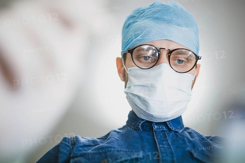 Surgeon wearing a blue cap and mask, focused on performing a medical task
