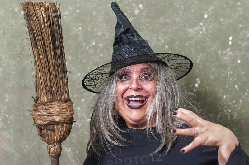 Old witch with white hair and a black hat with an ancient broom in her hands and a terrifying gesture