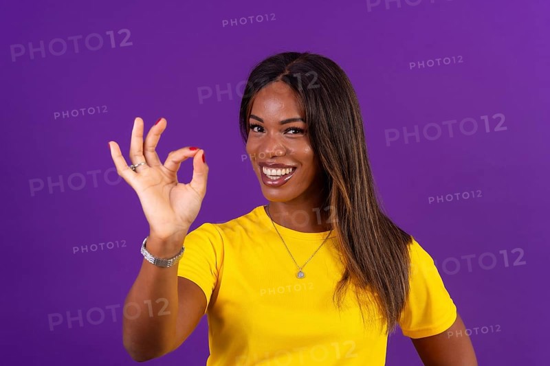 Studio portrait with purple background of an african smiling urban woman gesturing agreement with hand