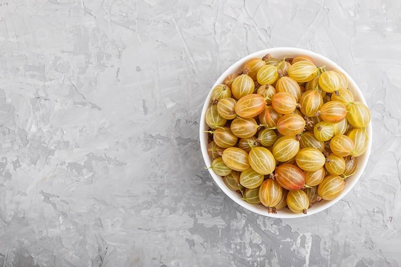 Fresh green gooseberry in white bowl on gray concrete background. top view, flat lay, copy space