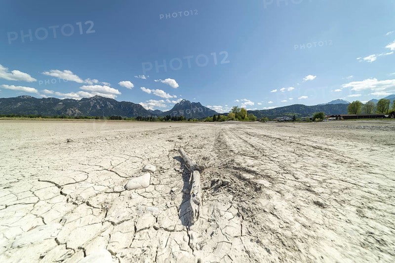 Cracked, dried out ground, waterless Forggensee in spring, behind it Tegelberg massif and Säuling, Ammergau Alps, near Füssen, Ostallgäu, Bavaria, Germany