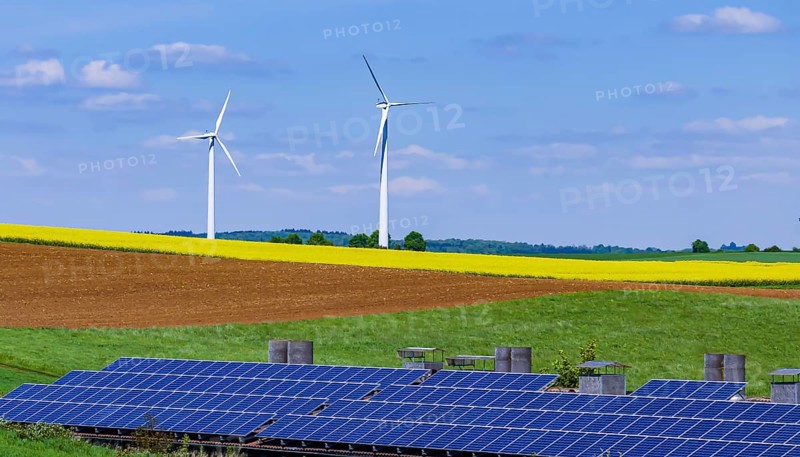 Landscape of the Swabian Alb in spring with rape field and wind turbines. In front of it a building with photovoltaic collectors. Dornstadt Baden-Württemberg, Germany