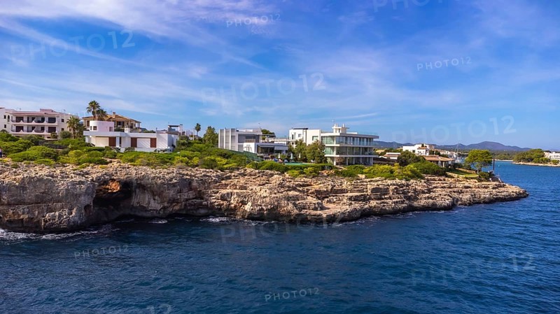 Stunning aerial view of the portocolom lighthouse and luxury villas perched on a rocky coastline in mallorca, spain, bathed in mediterranean sunlight