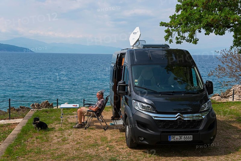 A campsite by the sea, a man sits next to a motorhome and enjoys the view with a dog, Glavotok, Krk island, Primorje-Gorski kotar, Croatia