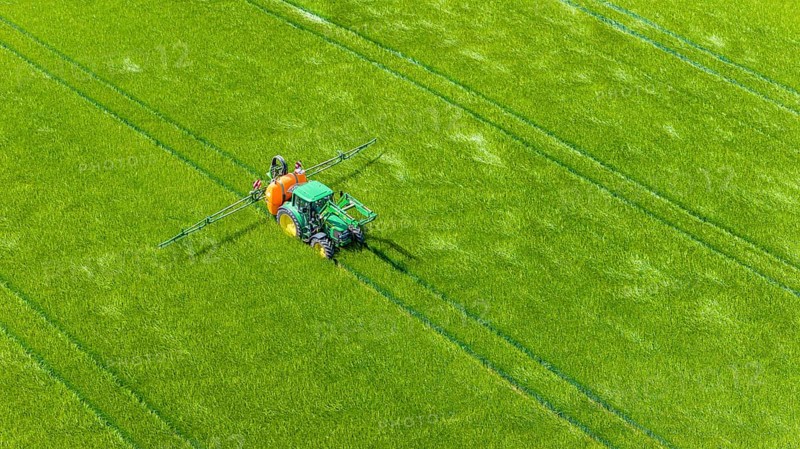 Farmer with tractor working in the field. In early summer, he fertilises the grain for an optimum yield. Drone photo. Merklingen, Baden-Württemberg, Germany