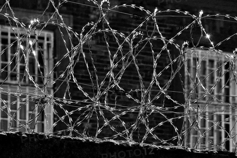 View through multiple coiled NATO wire onto the barred windows of Giessen Prison, Hesse, Germany