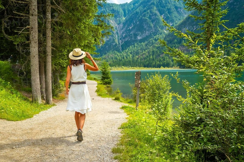 Tourist walking on a path near lake dobbiaco, enjoying the summer landscape in the dolomites