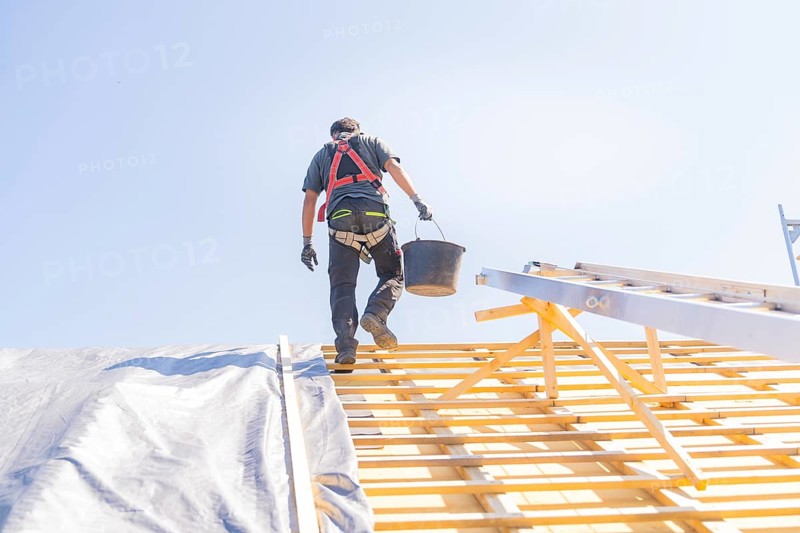 A worker in safety clothing climbs a ladder to work on a roof, in sunny weather, roof renovation, house construction, Pforzheim, Germany