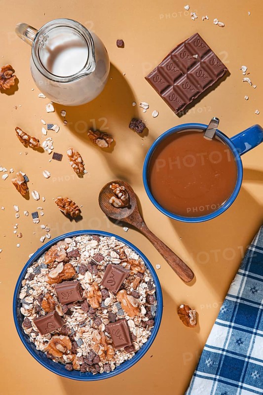 Breakfast, muesli with chocolate and walnuts next to milk and coffee from above on a yellow background