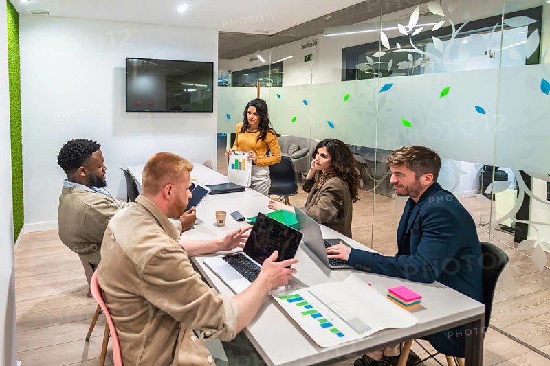Marketing managers collaborating on a project, analyzing charts and using laptops in a modern meeting room