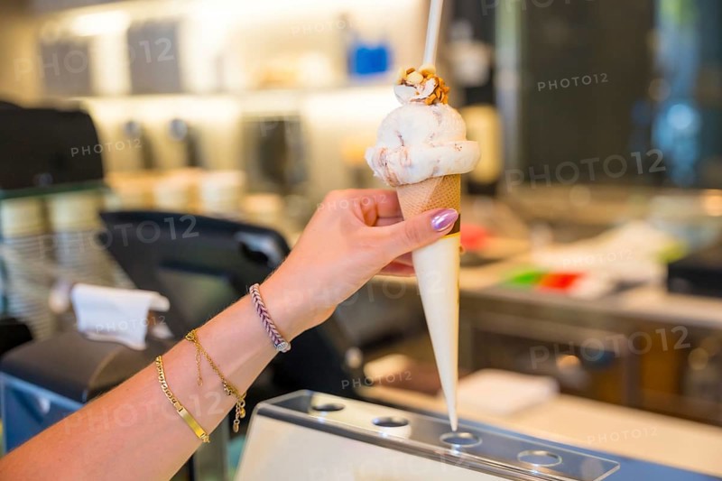 Womans hand adorned with bracelets, holding a delicious ice cream cone topped with crunchy nuts, enjoying a treat at a gelateria
