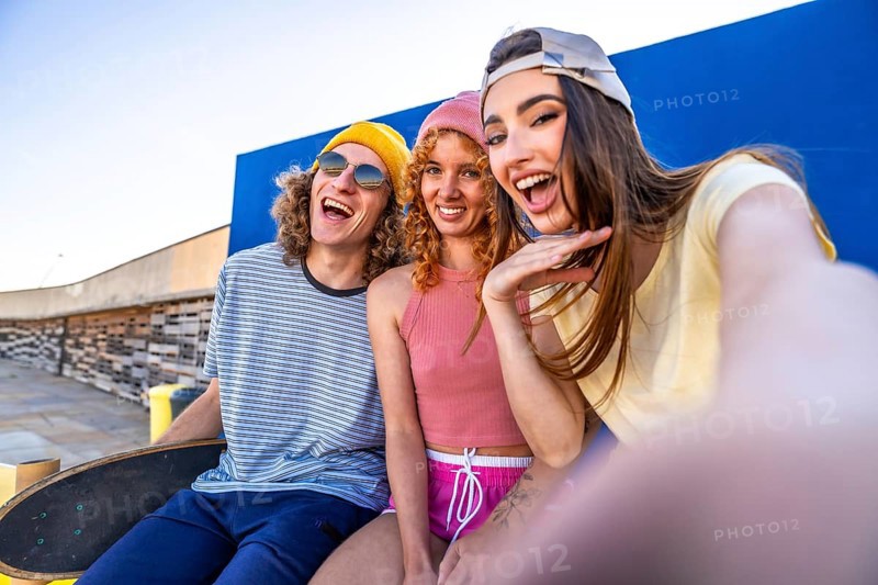 Three joyful skaters enjoying a sunny day, capturing a fun selfie against a vibrant blue wall, celebrating friendship and youthful energy