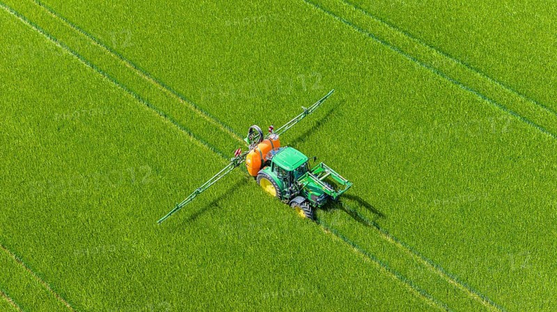 Farmer with tractor working in the field. In early summer, he fertilises the grain for an optimum yield. Drone photo. Merklingen, Baden-Württemberg, Germany